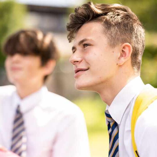 Happy male student outdoors with friend in background